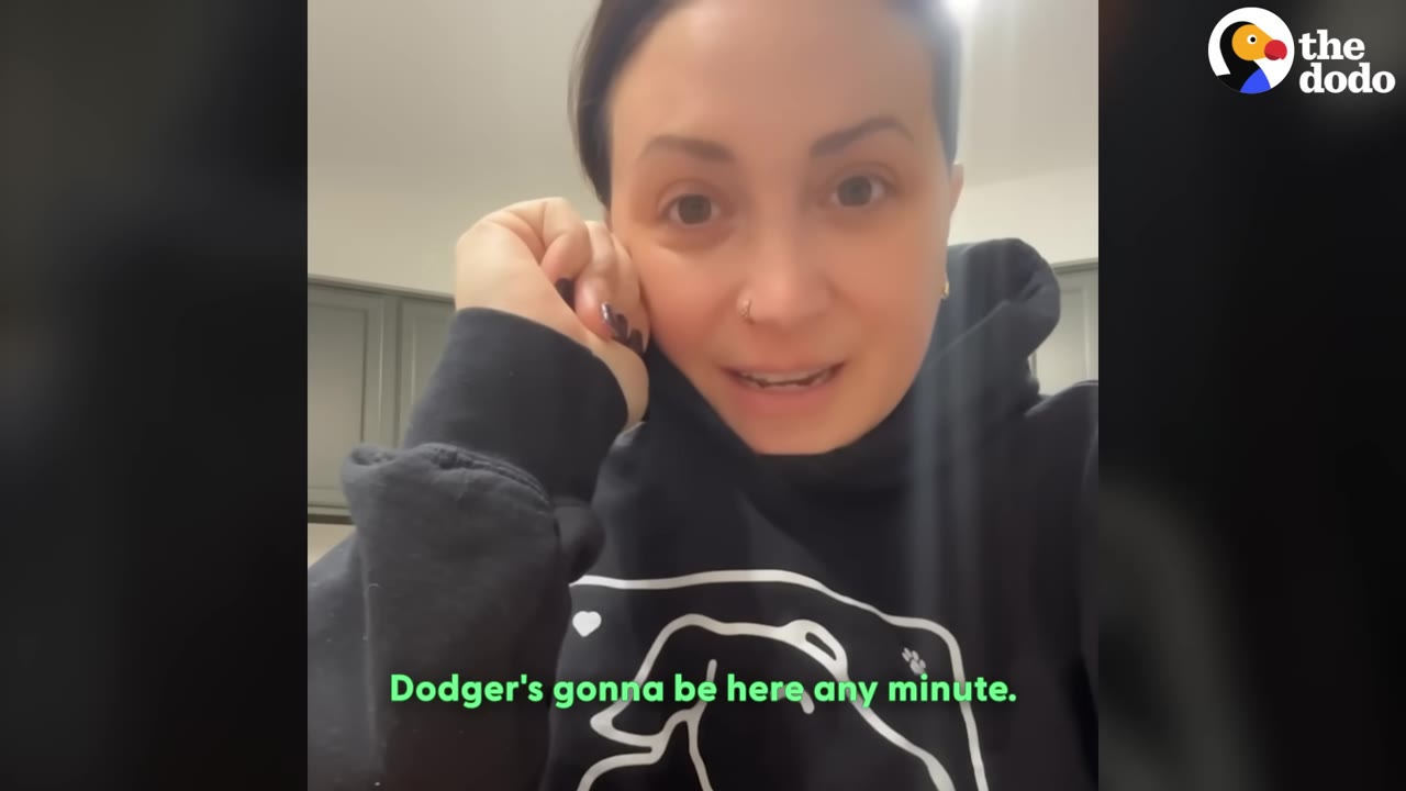 A woman wearing a black hoodie with a dog outline on it looks anxiously at the camera with her hand resting on her cheek, with the subtitle 'Dodger's gonna be here any minute.'