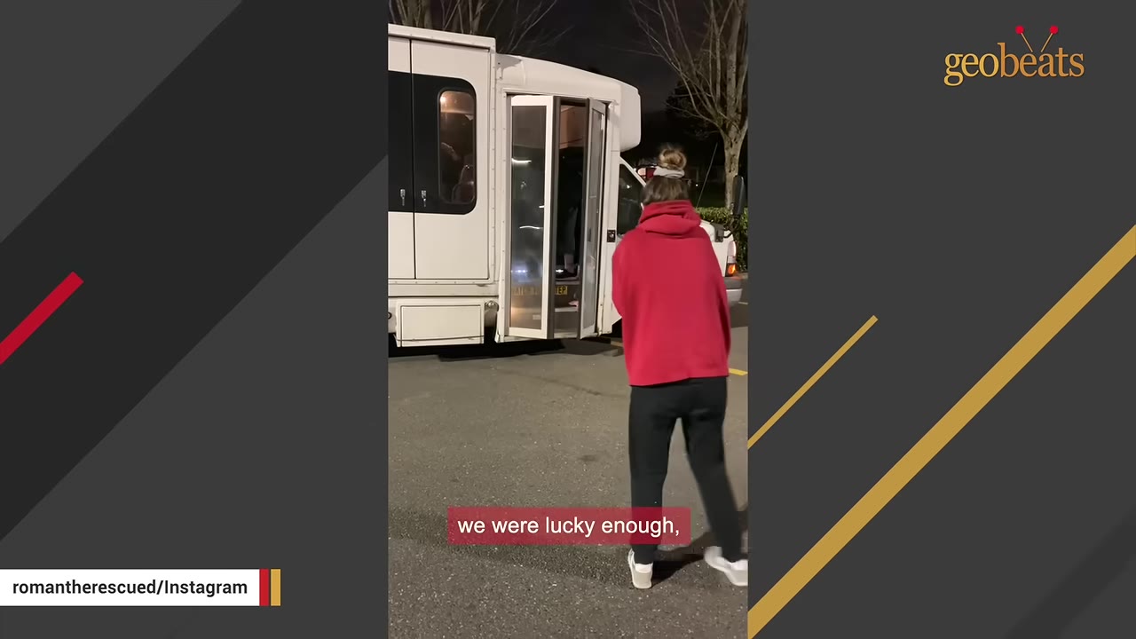 A person in a red hoodie and dark pants walks toward the open door of a white transport vehicle at night.
