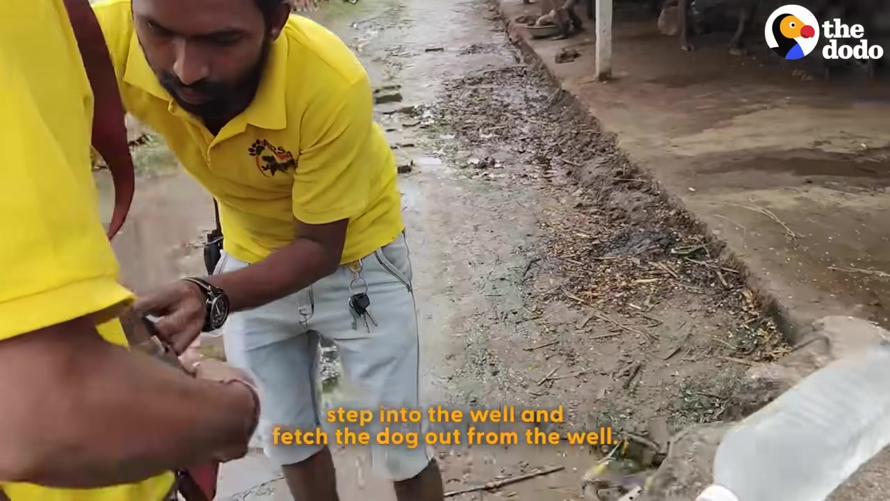 A rescuer in a yellow shirt and light-colored shorts prepares his gear near the edge of a brick well.