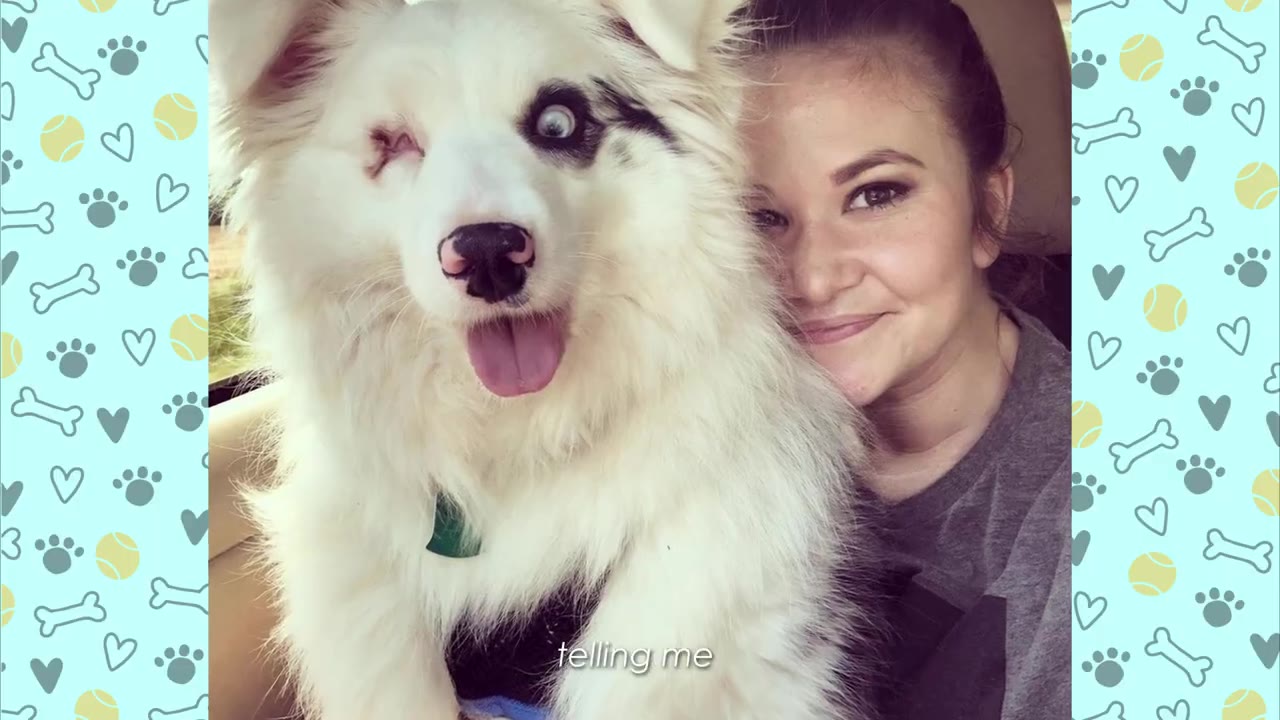 A smiling woman sits next to a fluffy white dog with one eye and its tongue sticking out.