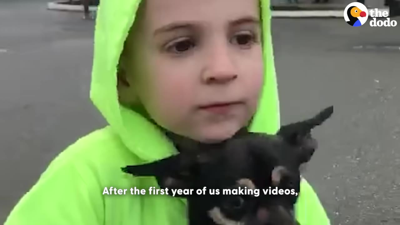 A young child wearing a bright neon green hooded sweatshirt holds a small black and tan dog close to their chest.
