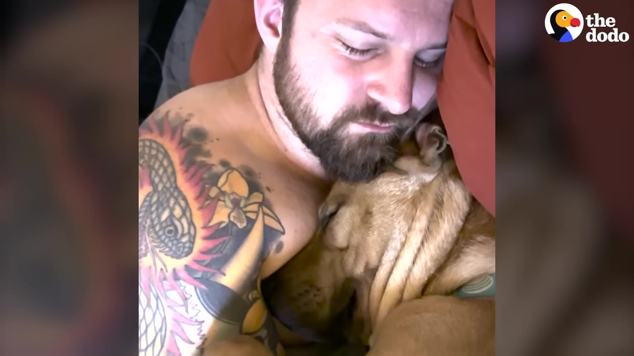 A tattooed man sleeping while cuddling a light brown dog close to his chest.