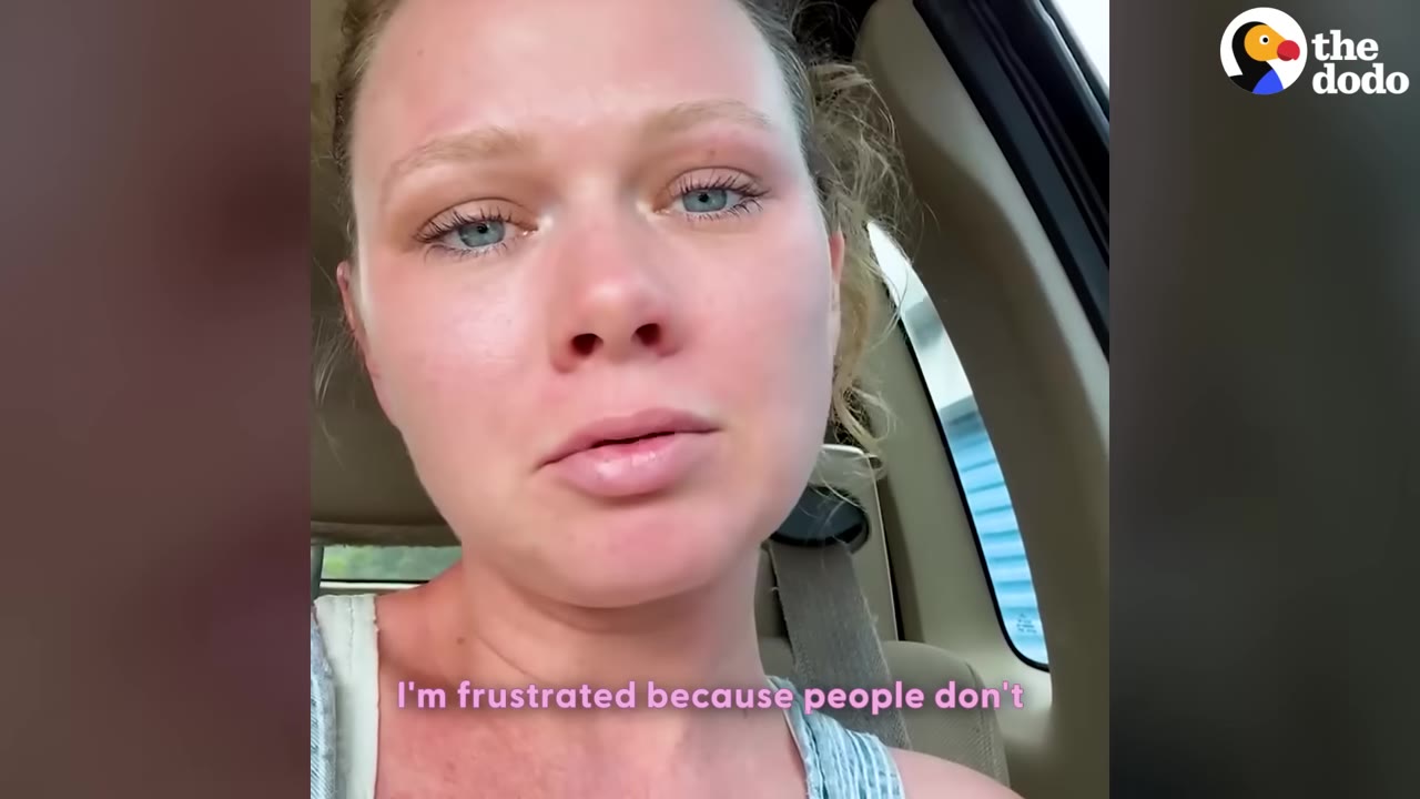 A close-up of a woman with blonde hair tied back, looking directly at the camera with a concerned and frustrated expression while sitting inside a vehicle.