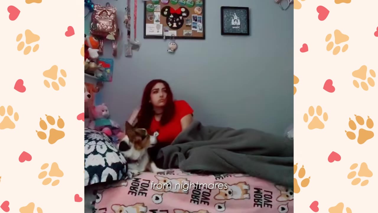 A young woman with red hair lies in bed under a grey blanket while her small Corgi dog sits beside her, looking up at her attentively.