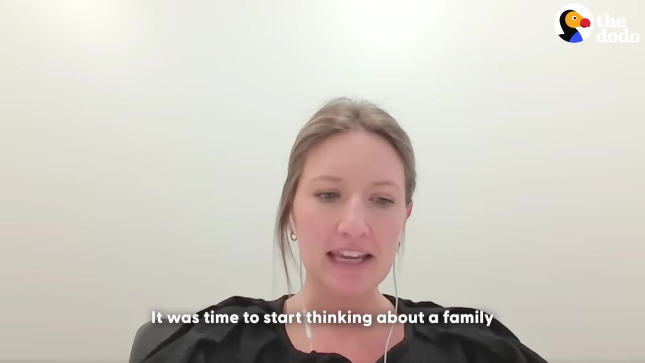 A woman with blonde hair tied back, wearing a black top and wired earbuds, speaking in front of a plain white wall with a subtitle that reads 'It was time to start thinking about a family'.