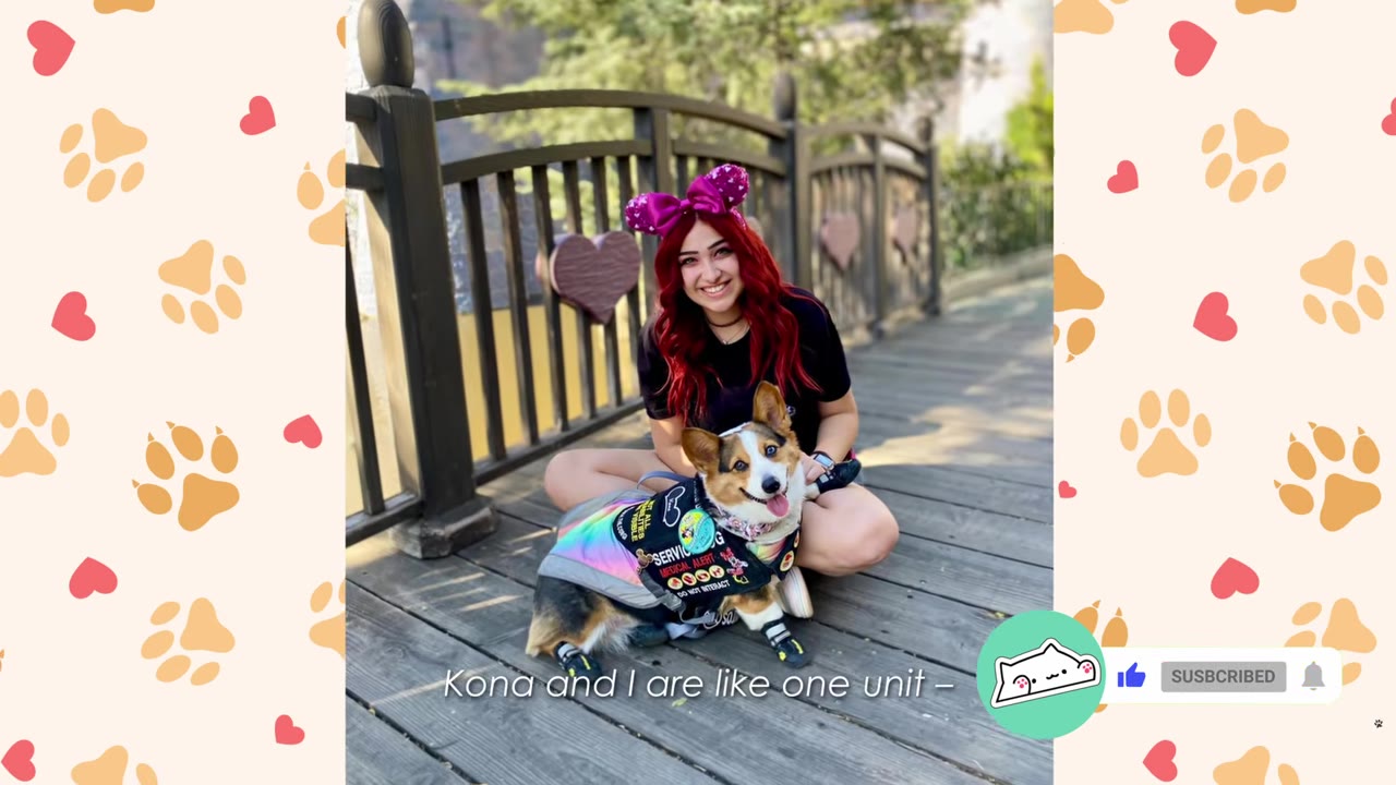 A smiling young woman with red hair wearing a pink bow headband sits on a wooden bridge next to her corgi service dog, who is wearing a colorful vest and booties.