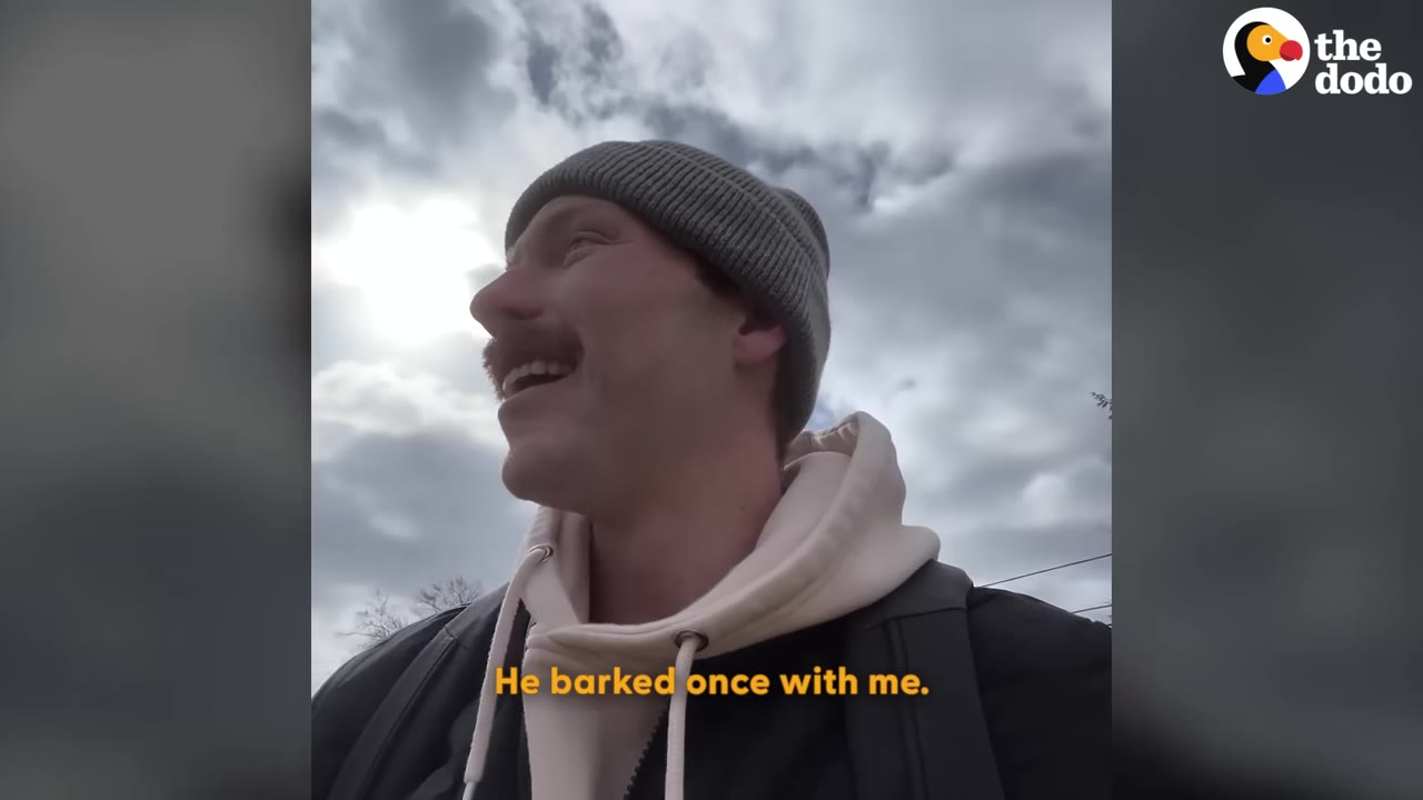 A man wearing a grey beanie and a white hoodie smiles against a cloudy sky, with the caption 'He barked once with me.'