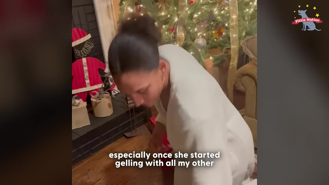 A woman with her hair in a bun, wearing a white robe, looks down with a Christmas tree in the background.