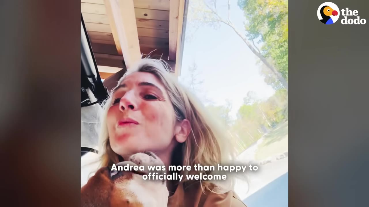 A close-up shot of Andrea smiling as a brown and white dog nuzzles her chin outdoors.