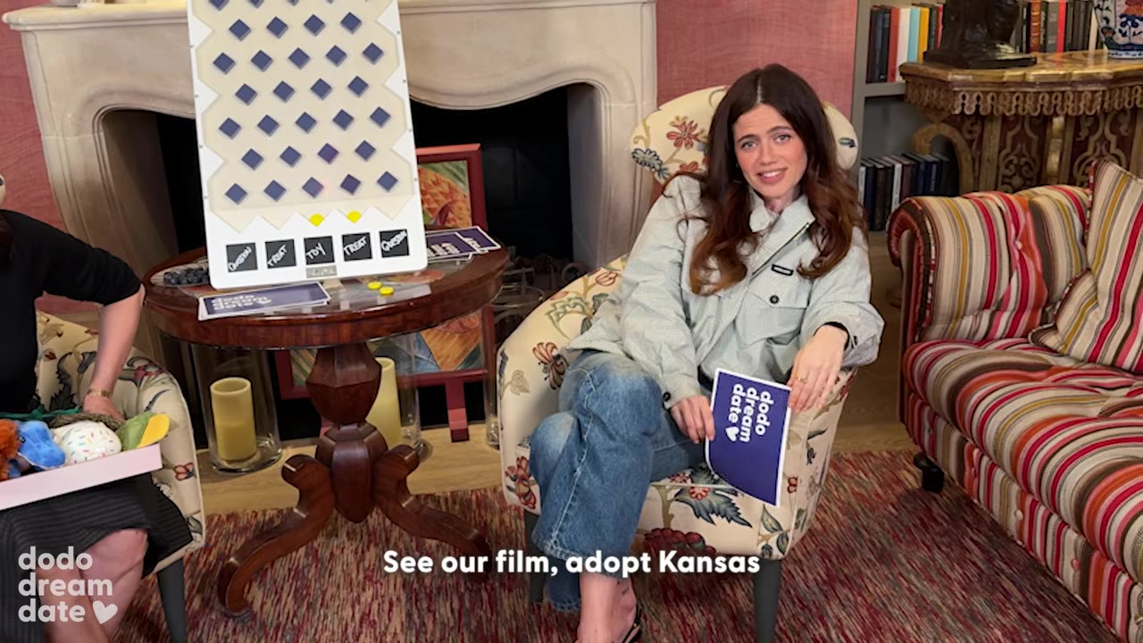A woman sitting in a floral armchair holding a blue card, with text on screen reading "See our film, adopt Kansas".