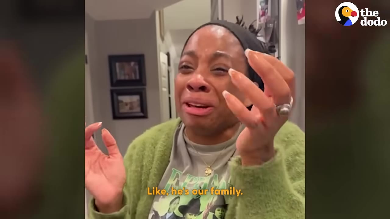 A woman wearing a green cardigan and a black headband cries with emotion, holding her hands up in disbelief.