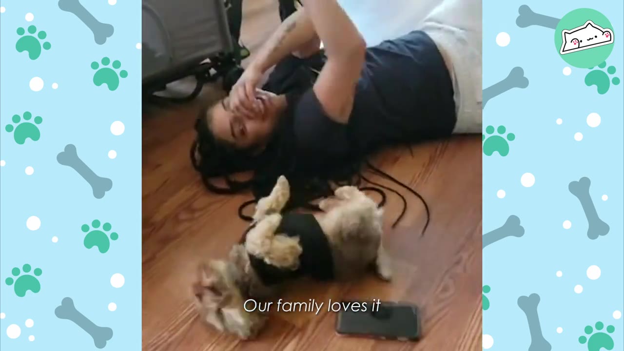 A woman lies on a wooden floor laughing next to a small, fluffy dog lying on its back.