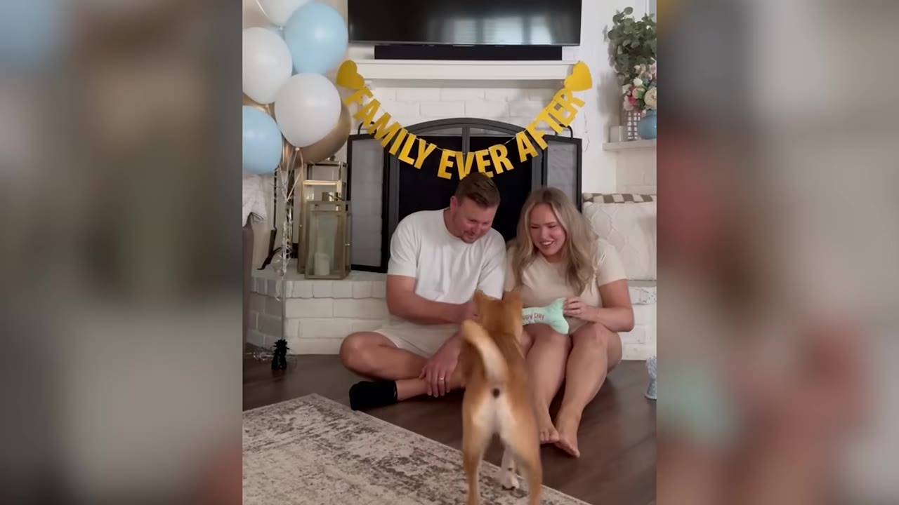 A man and a woman sit on the floor in front of a fireplace decorated with balloons and a banner that reads 'FAMILY EVER AFTER', smiling as a light brown dog stands in front of them.