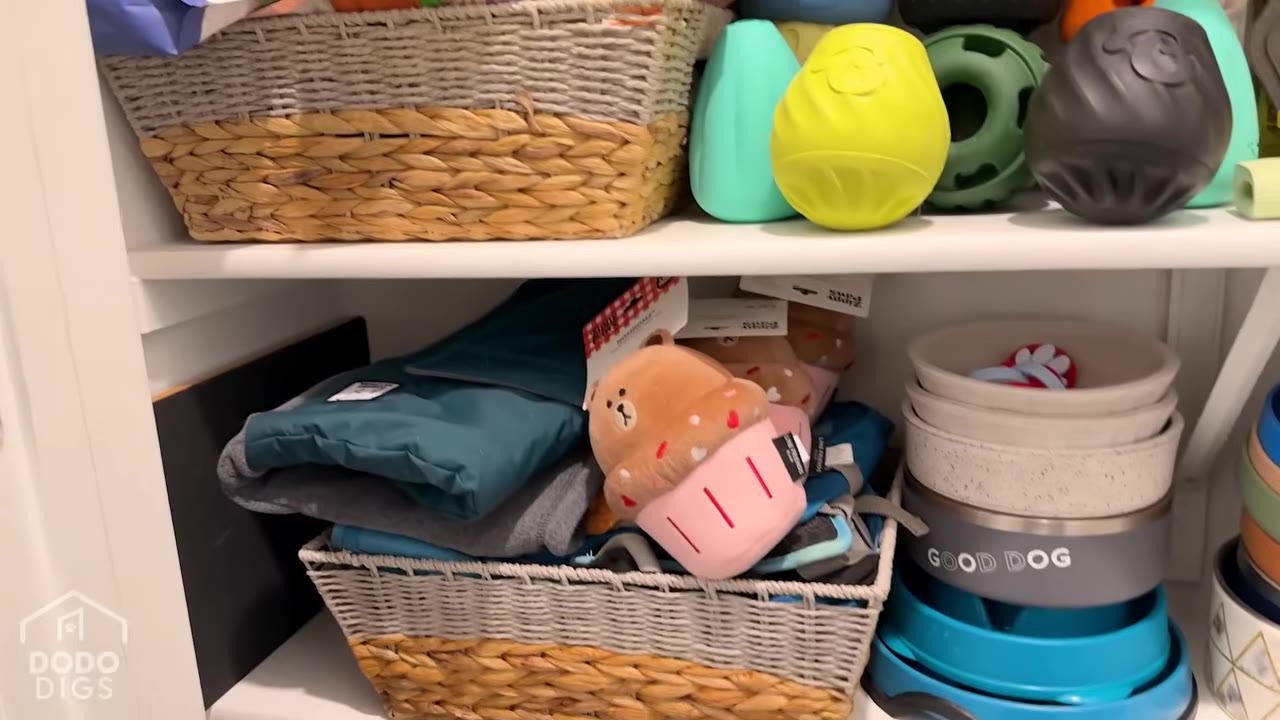 A plush cupcake toy sits in a woven basket on a closet shelf filled with dog toys and bowls.