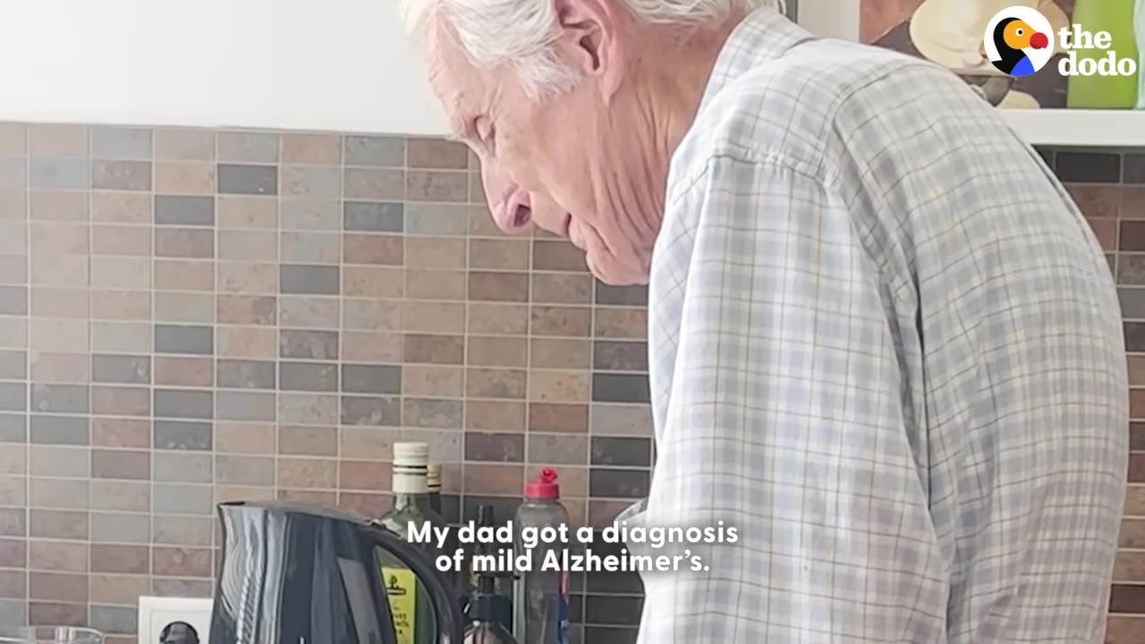 A side profile of an elderly man with white hair wearing a plaid shirt, looking down in a kitchen setting.