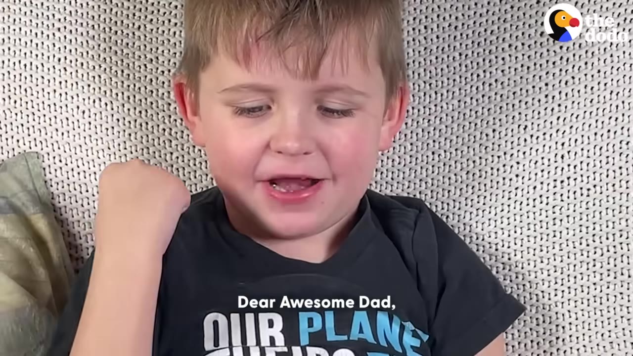 A young boy with light brown hair looks down and speaks, with the subtitle 'Dear Awesome Dad,' displayed on his dark t-shirt.