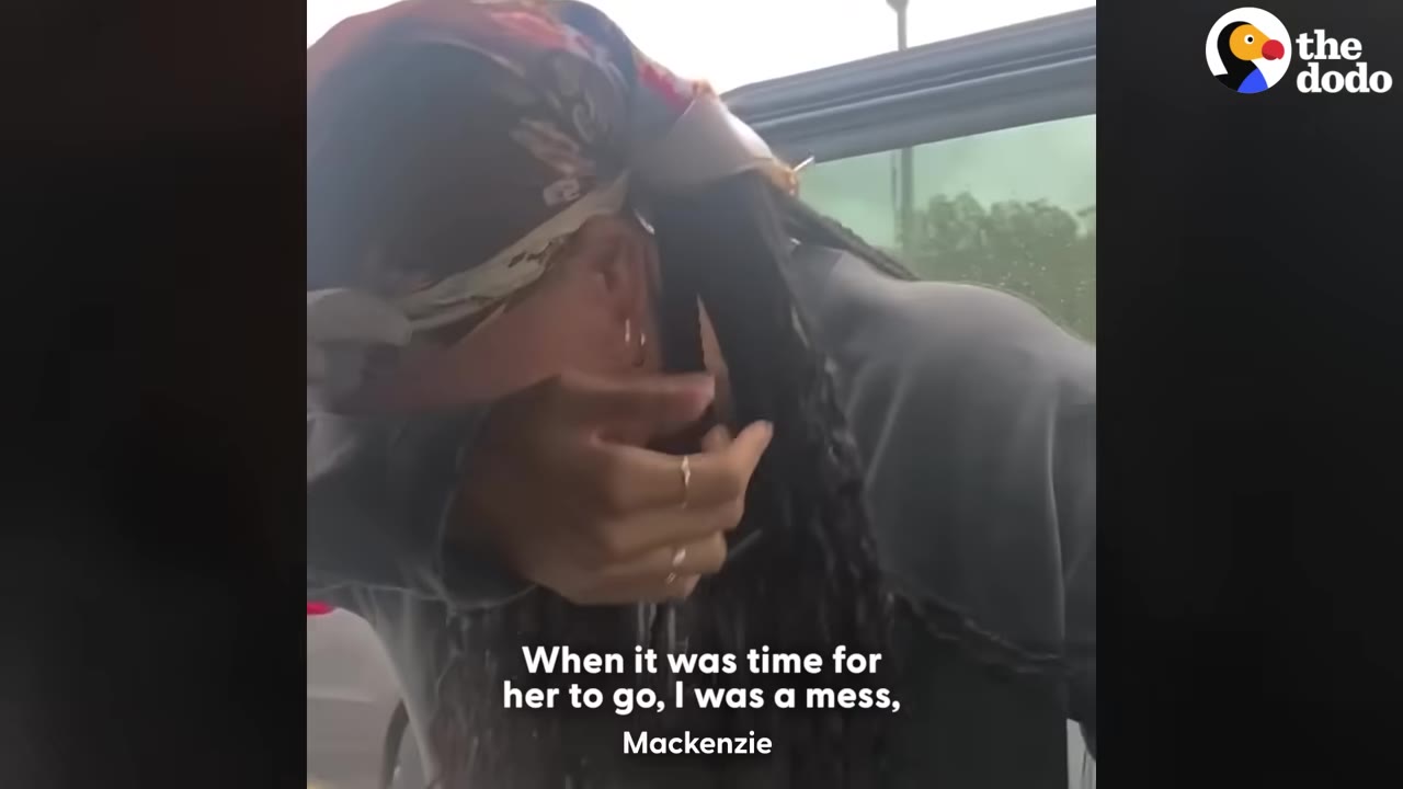 A woman wearing a patterned headscarf wipes tears from her face while crying inside a vehicle.