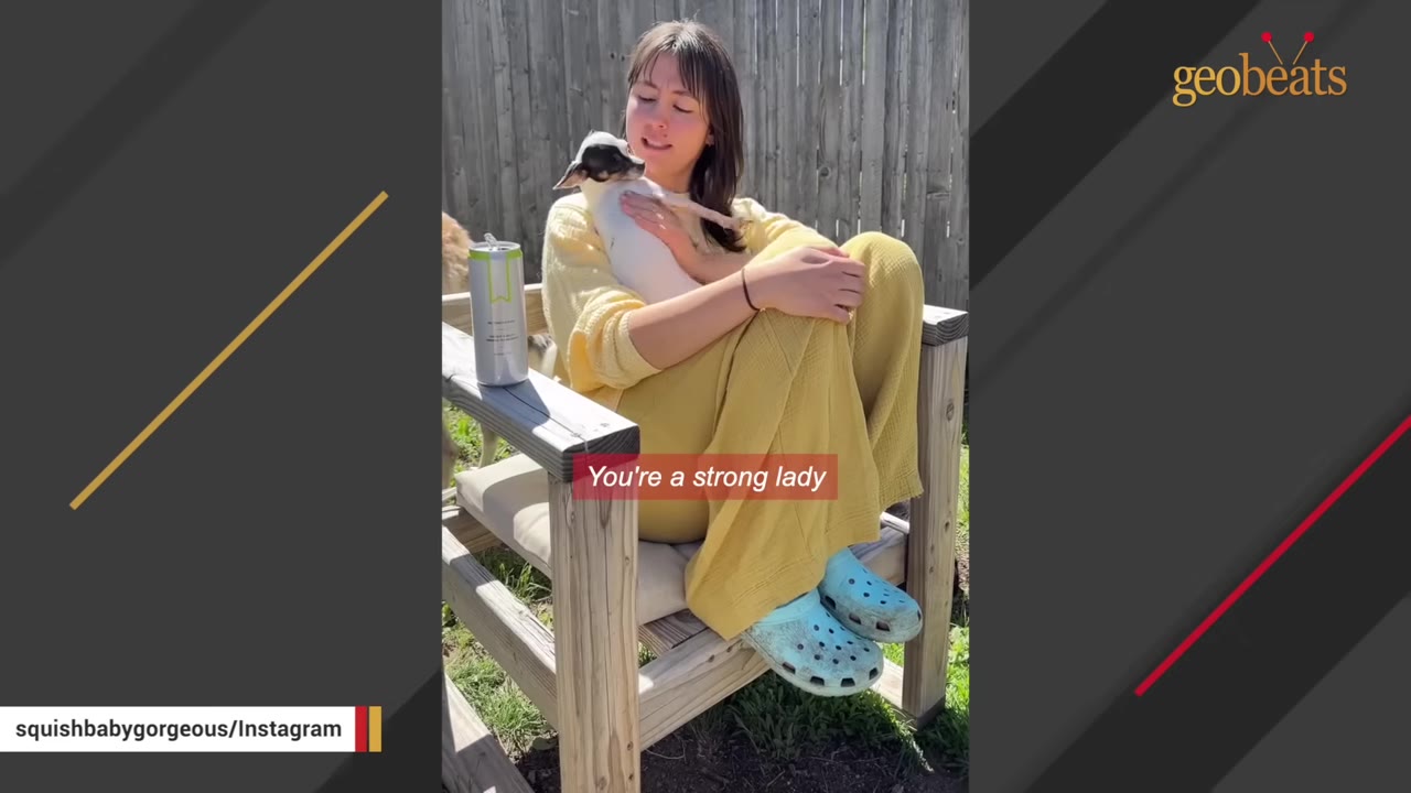 A woman in a yellow sweater sits in a wooden chair outdoors, holding a small white and black dog close to her chest.