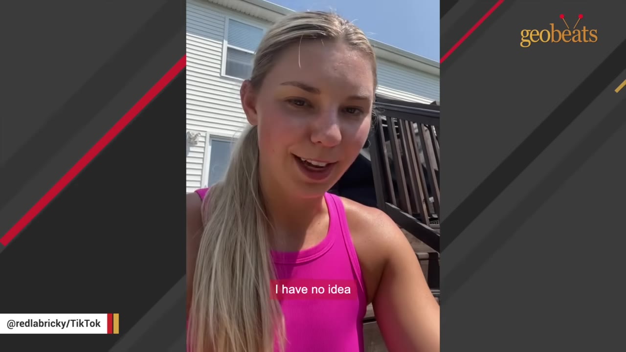 A young woman with blonde hair in a ponytail and a pink top speaks outdoors in front of a house.