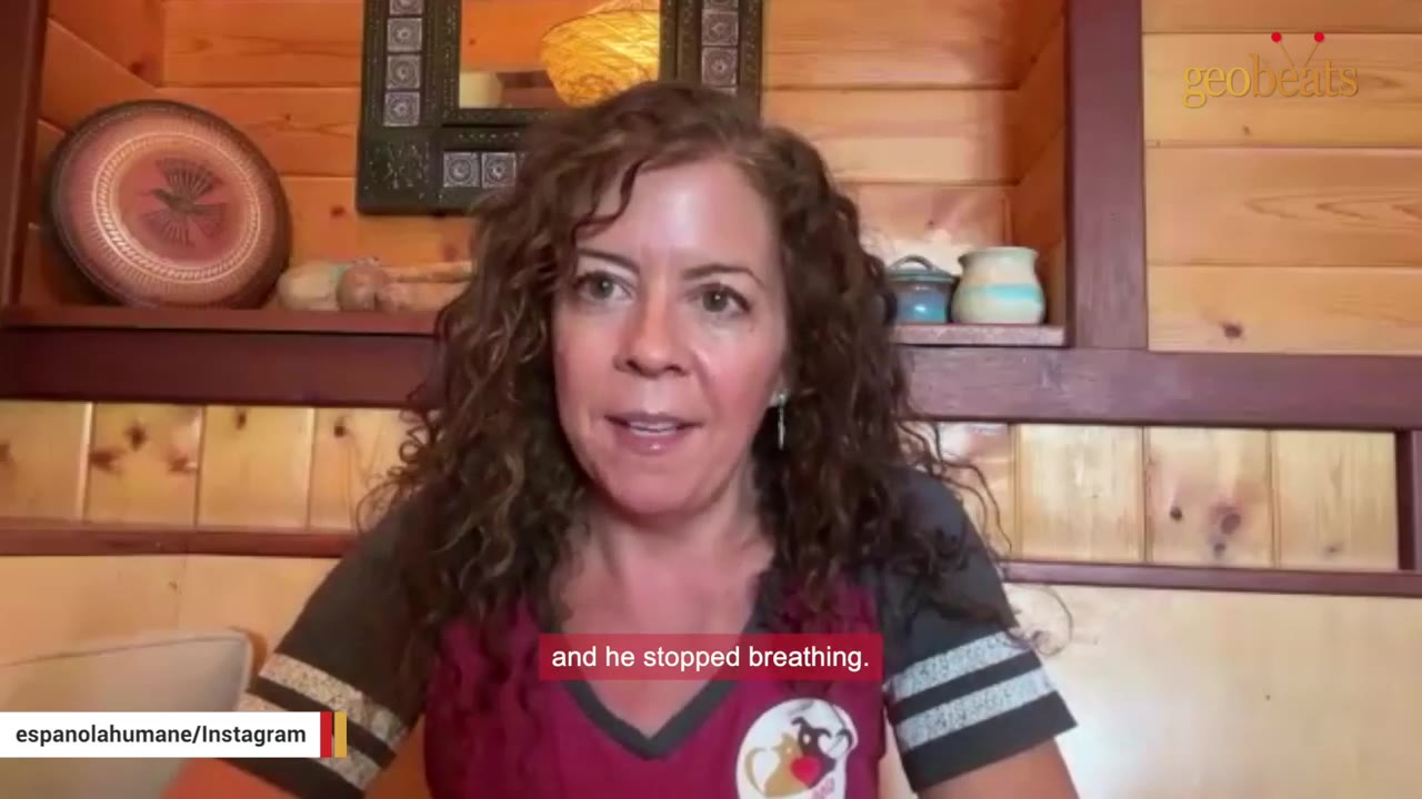 A woman with curly brown hair speaks to the camera in front of a wooden wall, with a subtitle reading 'and he stopped breathing.'