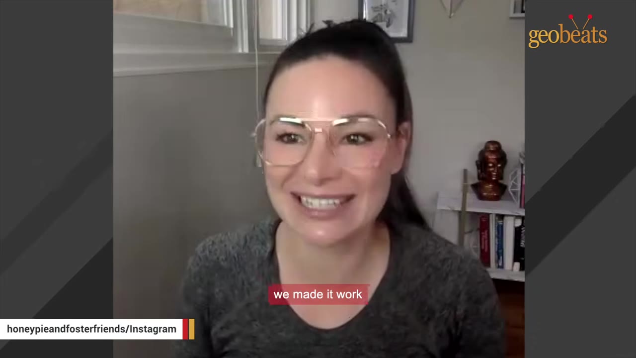 A woman with dark hair tied back and wearing clear-framed glasses smiles while speaking in front of a neutral background.