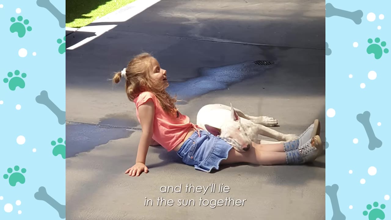 A young girl in a pink shirt and denim skirt sits on a sunny concrete driveway, leaning back with a white bull terrier resting its head on her lap.