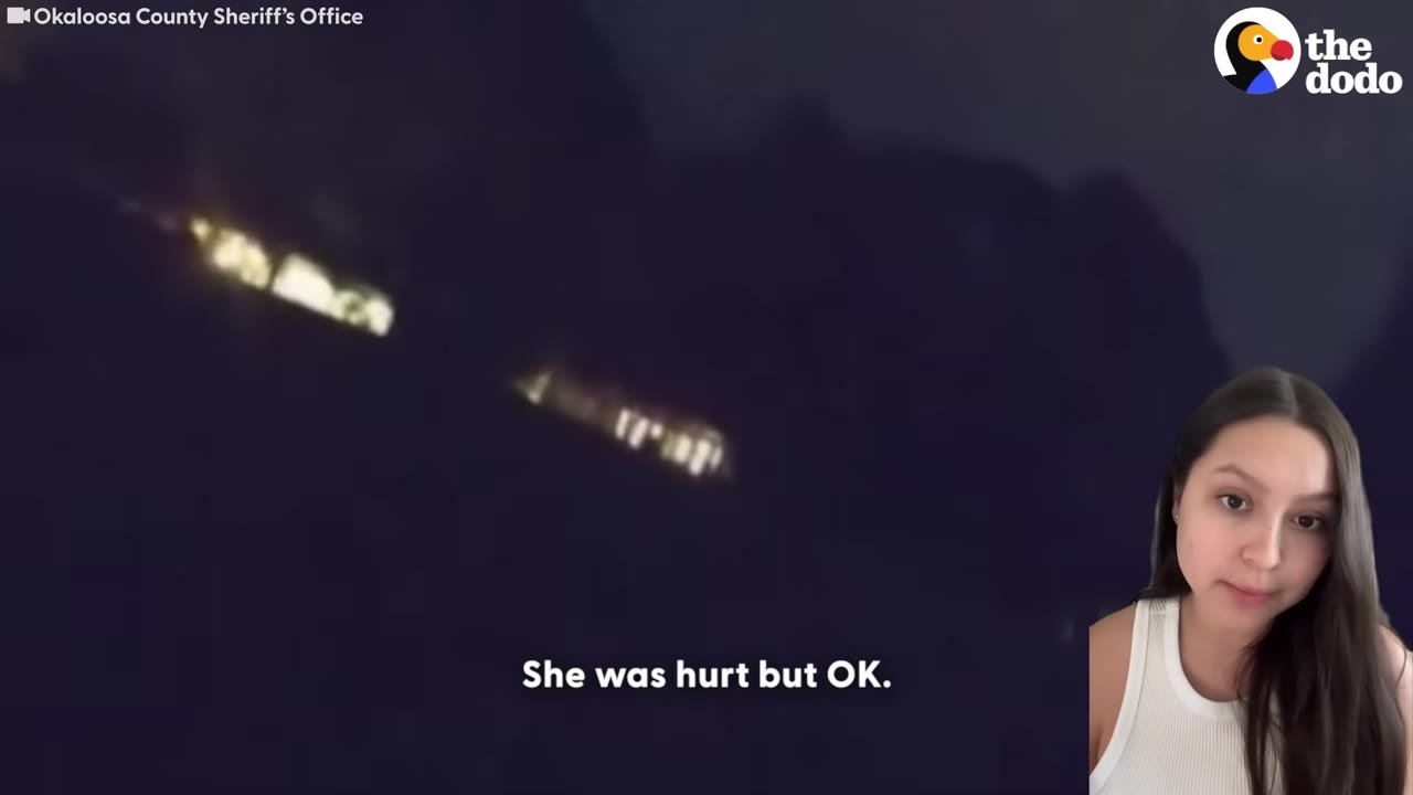 A dark night scene with distant lights on a hillside, featuring a split-screen of a woman speaking on the right and subtitles that read 'She was hurt but OK.'