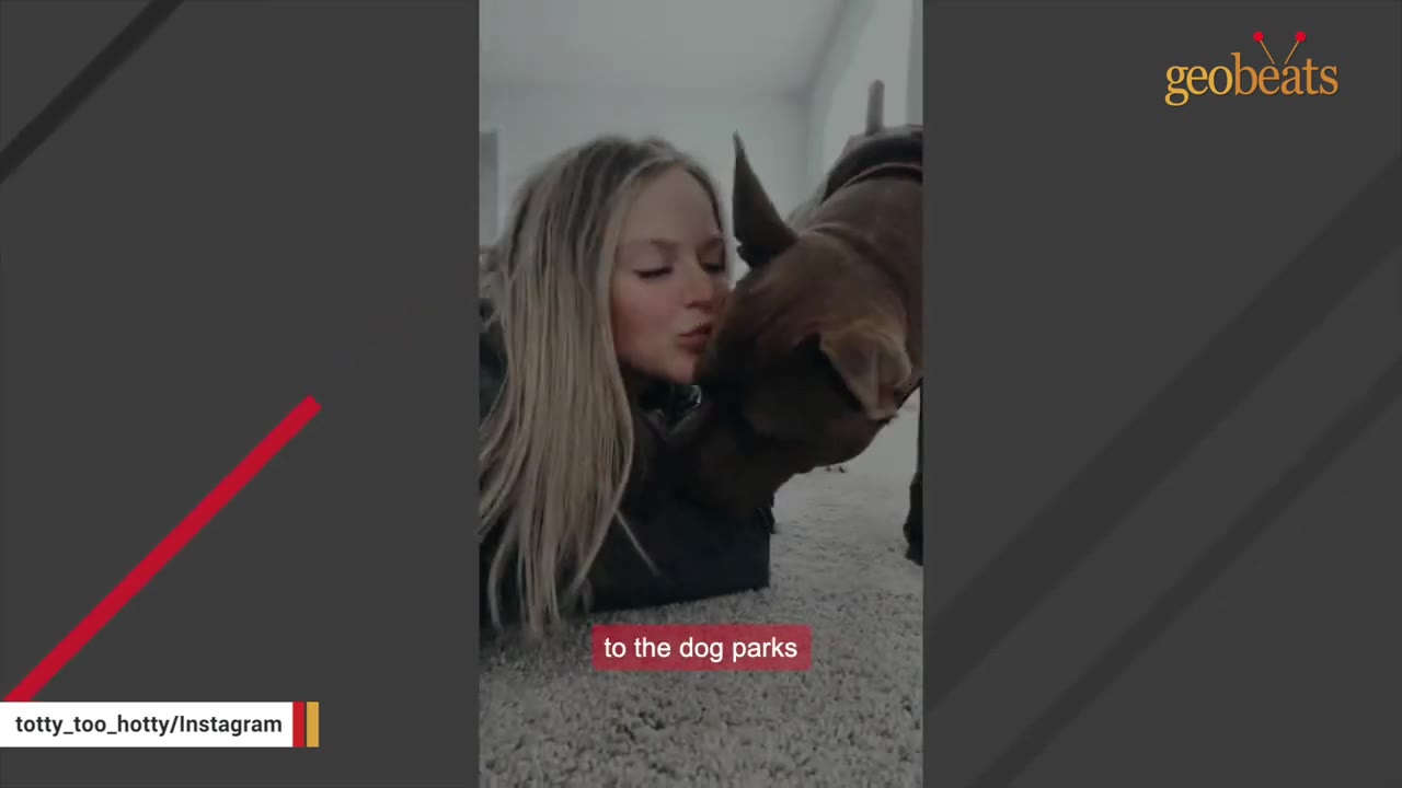 A blonde woman lies on a carpeted floor, leaning in to kiss a brown dog.
