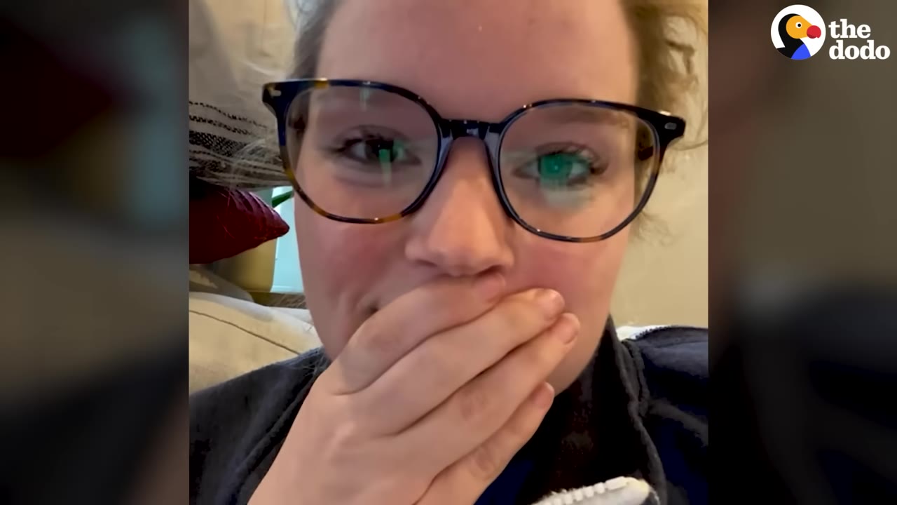 A close-up of a woman wearing glasses, looking surprised with her hand covering her mouth.