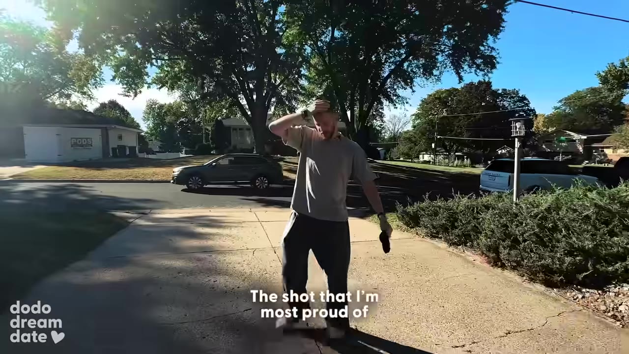 A man in a grey t-shirt and dark pants stands on a sunny driveway, wiping his forehead with his hand while reflecting on his proudest shot.