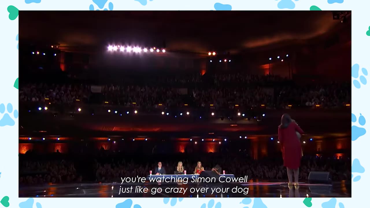 A wide shot of a woman in a red dress performing on a large, dimly lit stage in front of a panel of four judges and a massive theater audience.