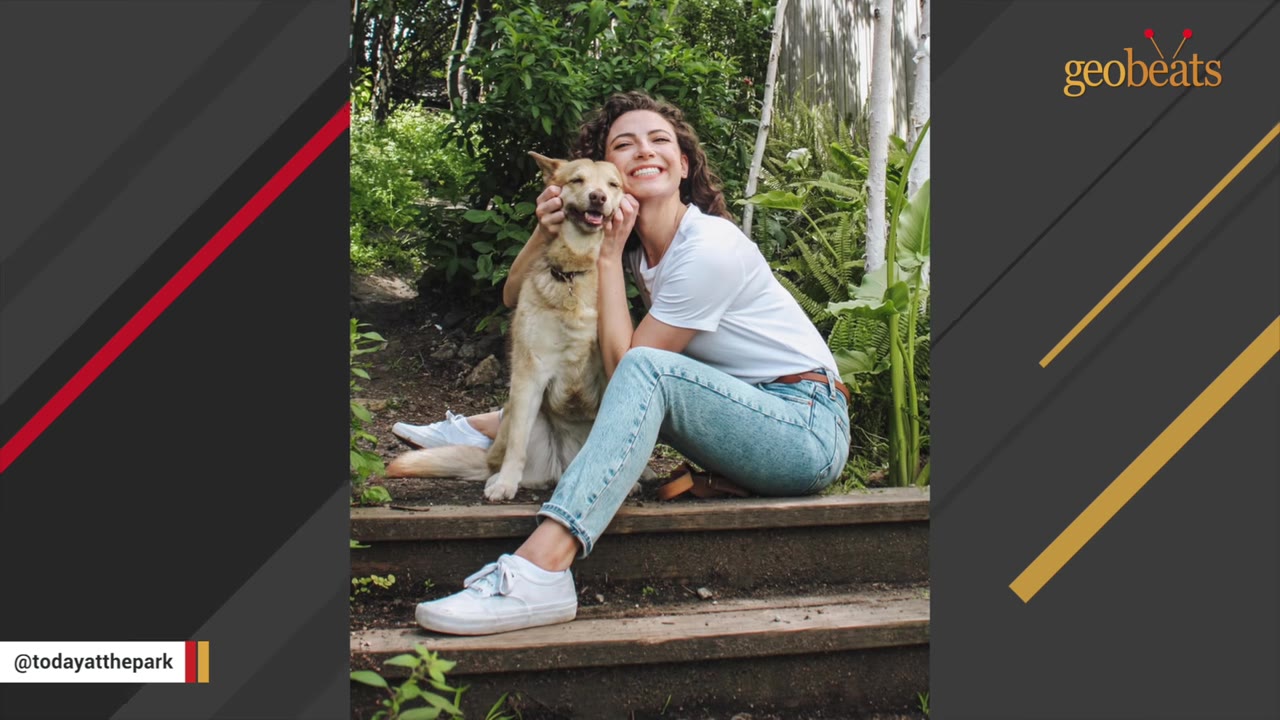 A smiling woman with curly hair sits on wooden steps outdoors, hugging her light-colored dog who also appears to be smiling.