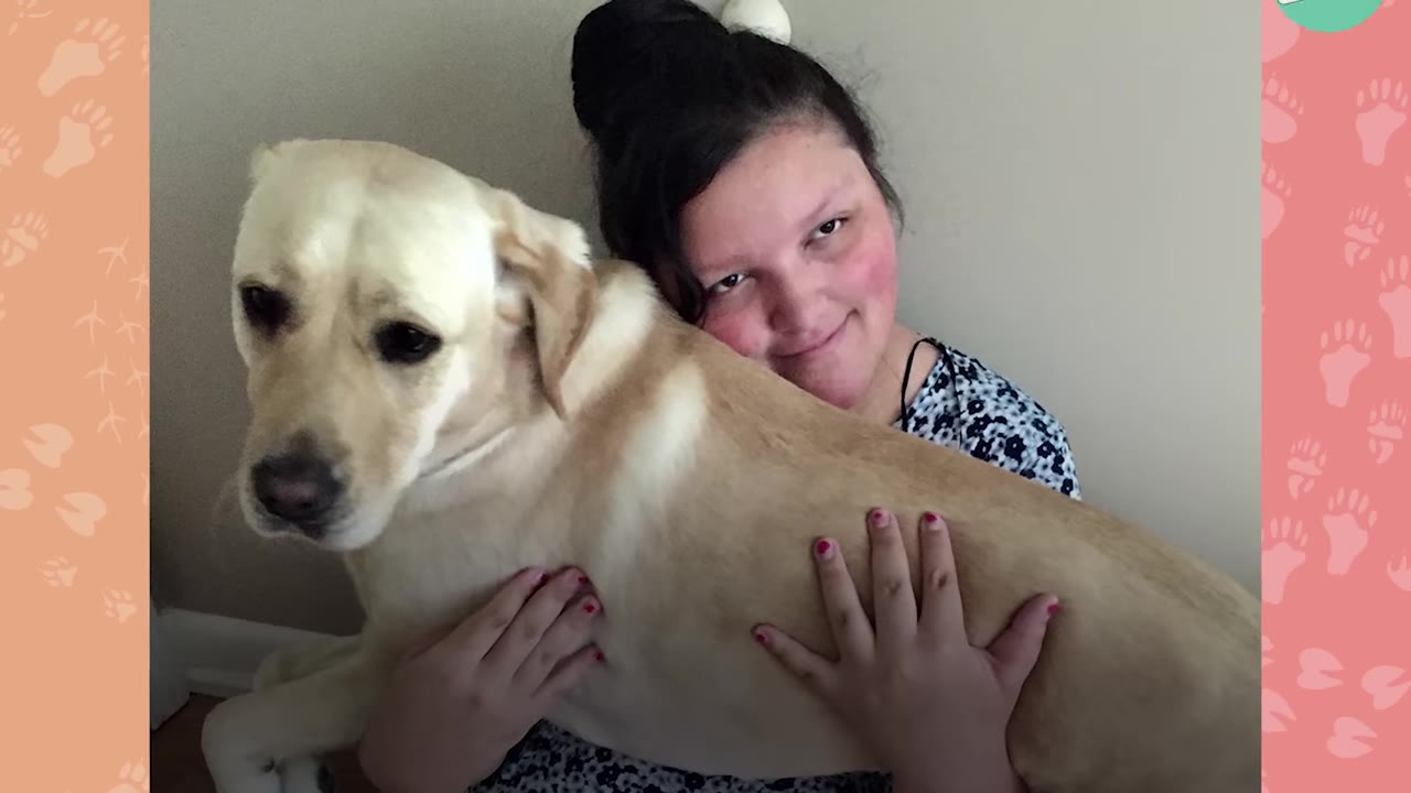 A young woman with dark hair tied up smiles as she hugs a yellow Labrador retriever.