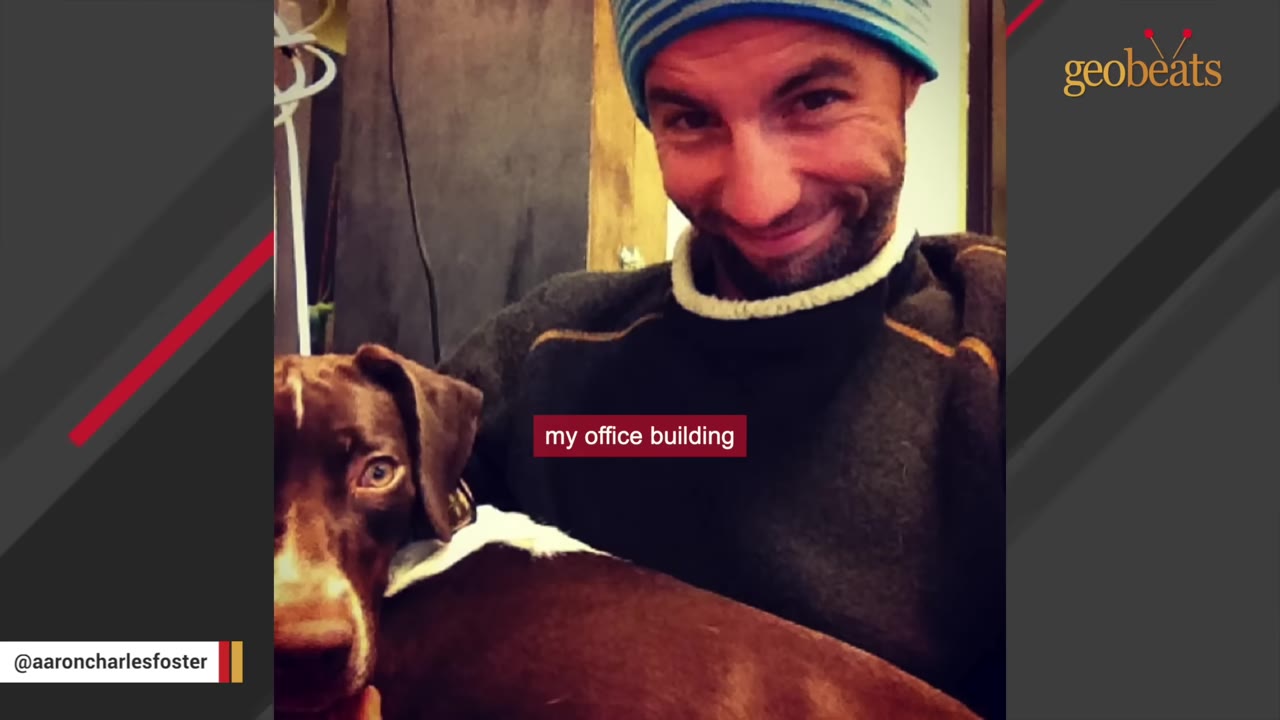 A man wearing a blue and white striped winter beanie and a dark sweater smiles next to a brown and white dog.