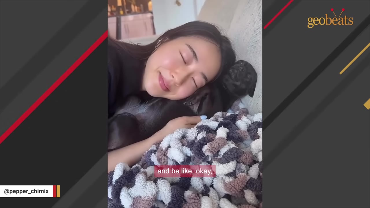 A young woman with her eyes closed smiles as she cuddles with a small black dog on a textured blanket.