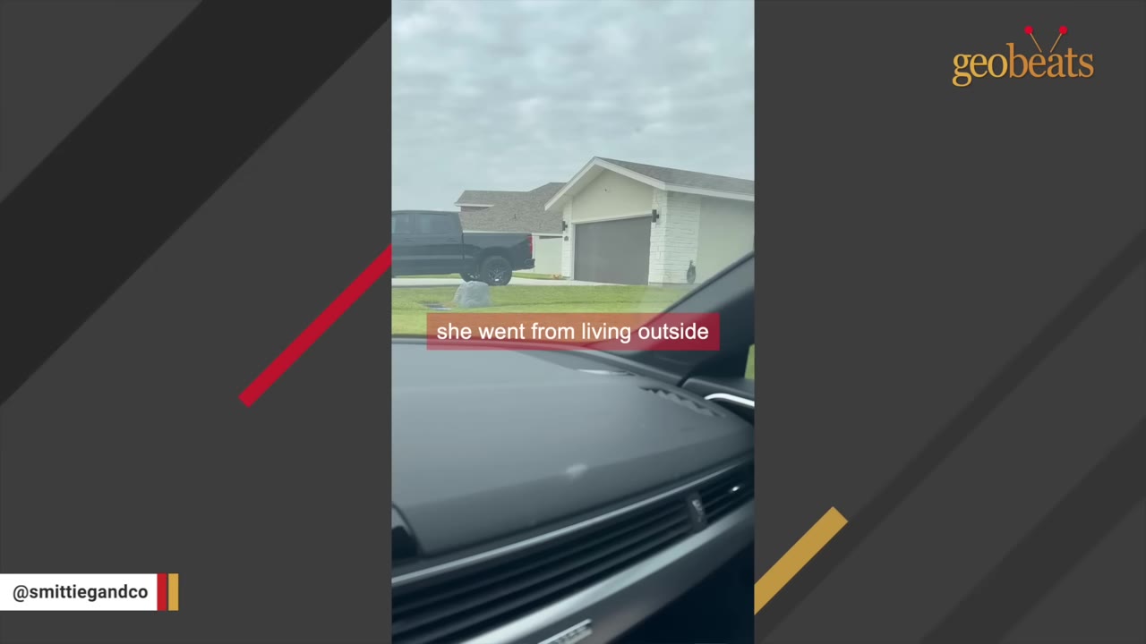 A view from inside a car looking out at a suburban house with a garage and a black pickup truck parked in the driveway.