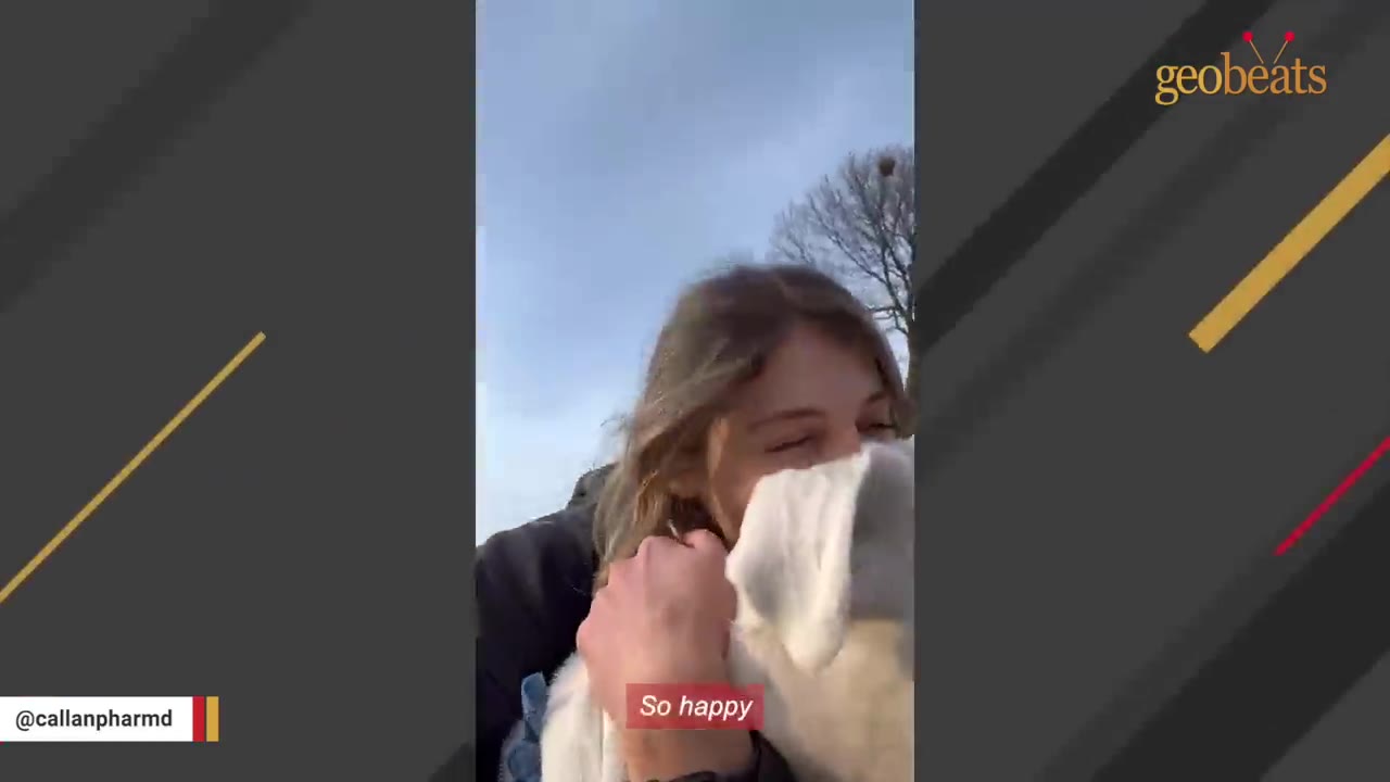 A woman smiling and hugging a white dog outdoors against a blue sky.