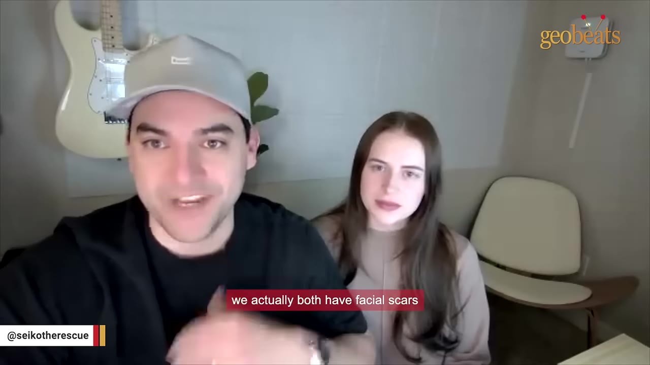 A man wearing a grey cap and a woman with long brown hair speaking to the camera, with a subtitle reading 'we actually both have facial scars'.