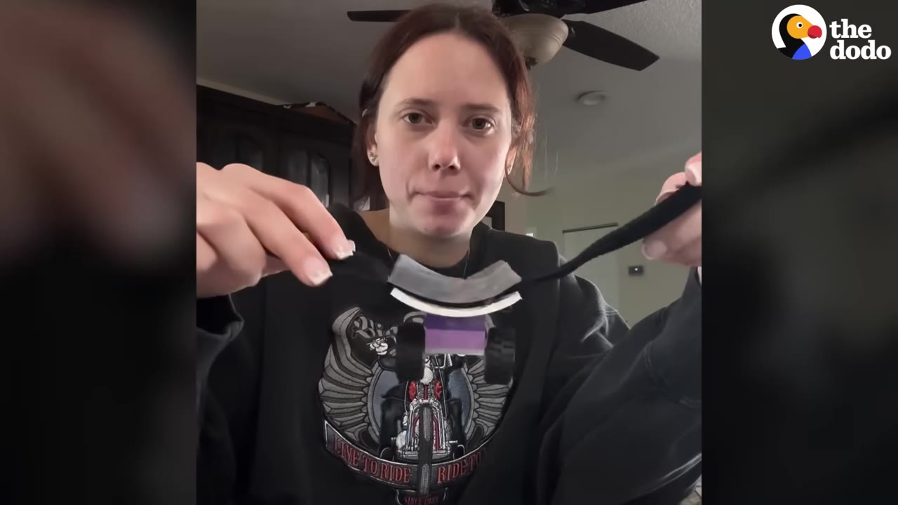 A woman holds up a small homemade device made of LEGO wheels, a purple block, and a black strap.