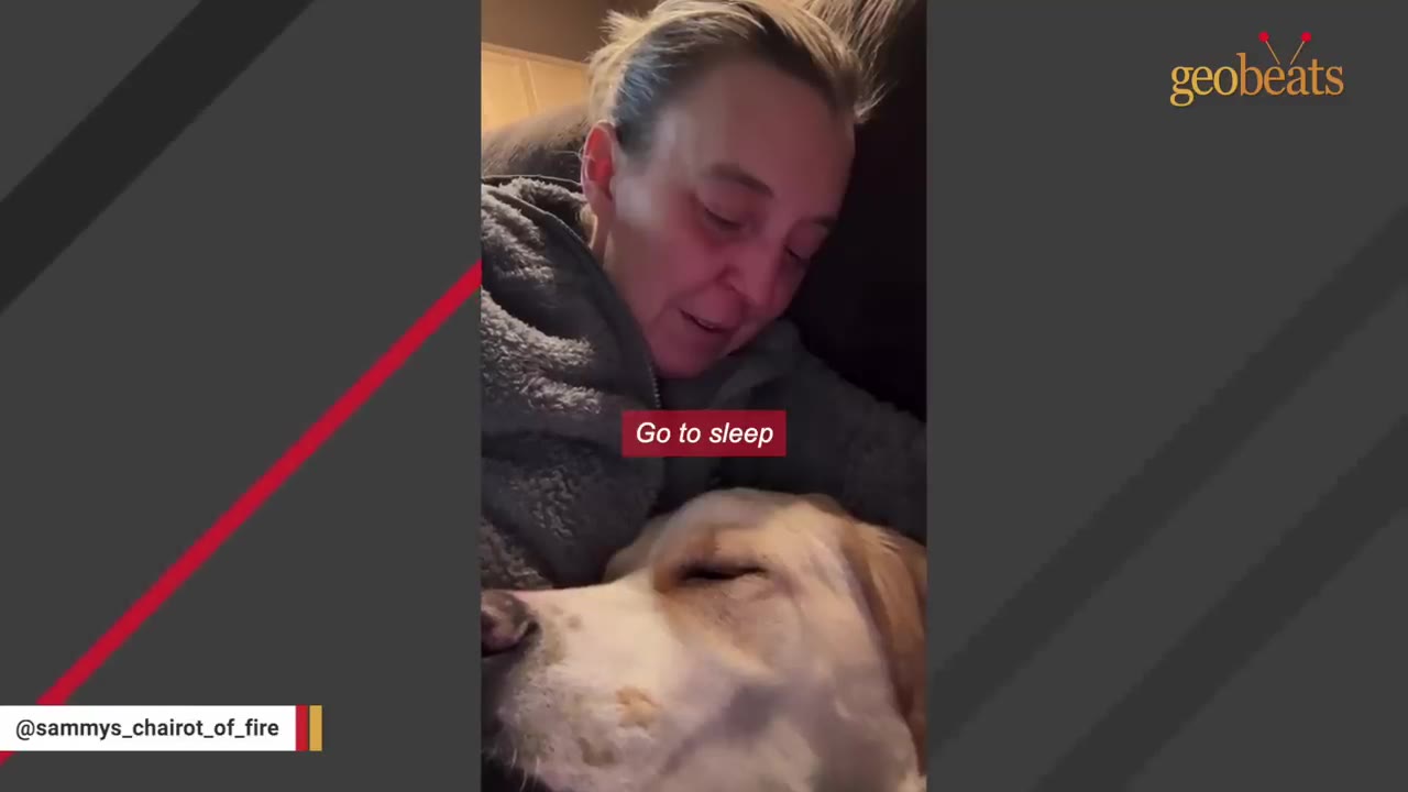 A woman looks down with a sad, concerned expression as she rests next to a sleeping light-colored dog.