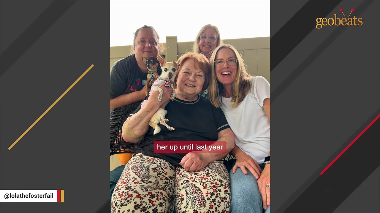 An older woman with reddish hair smiles while holding a small white chihuahua wearing a pink collar, surrounded by three other smiling women outdoors.