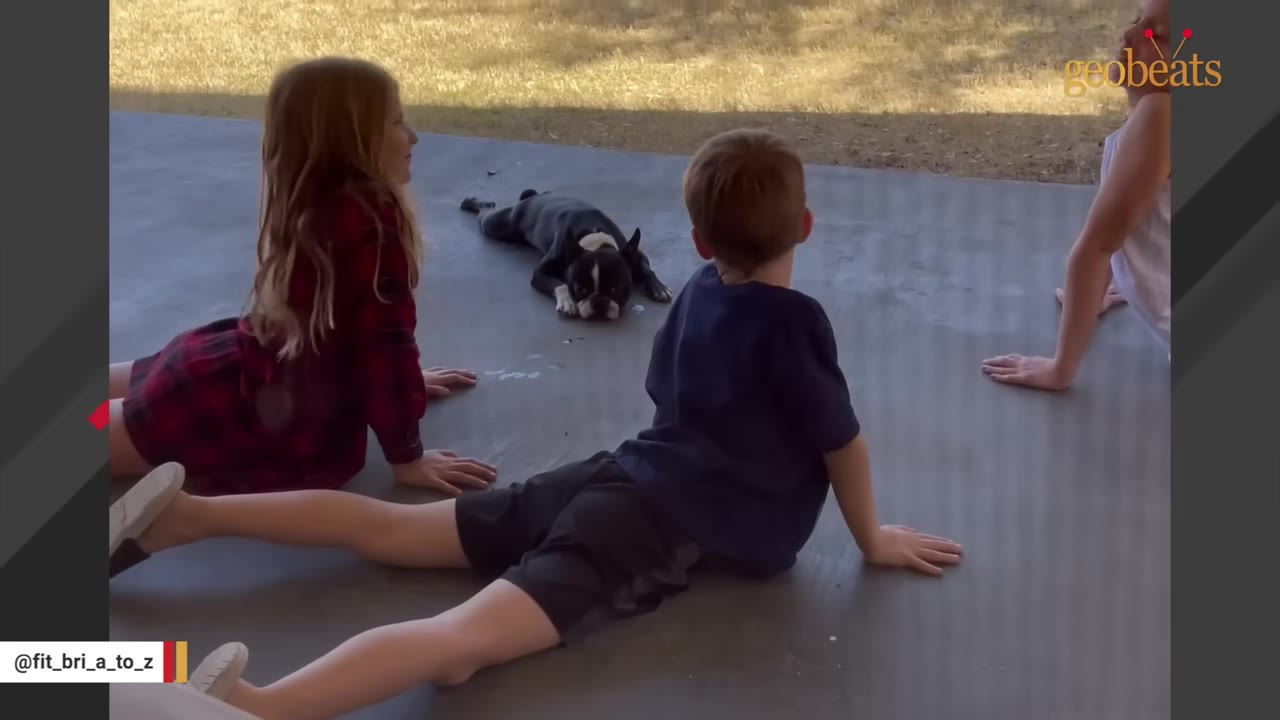 Three children doing cobra yoga poses on a concrete patio while a black and white Boston Terrier lies flat on its belly facing them.