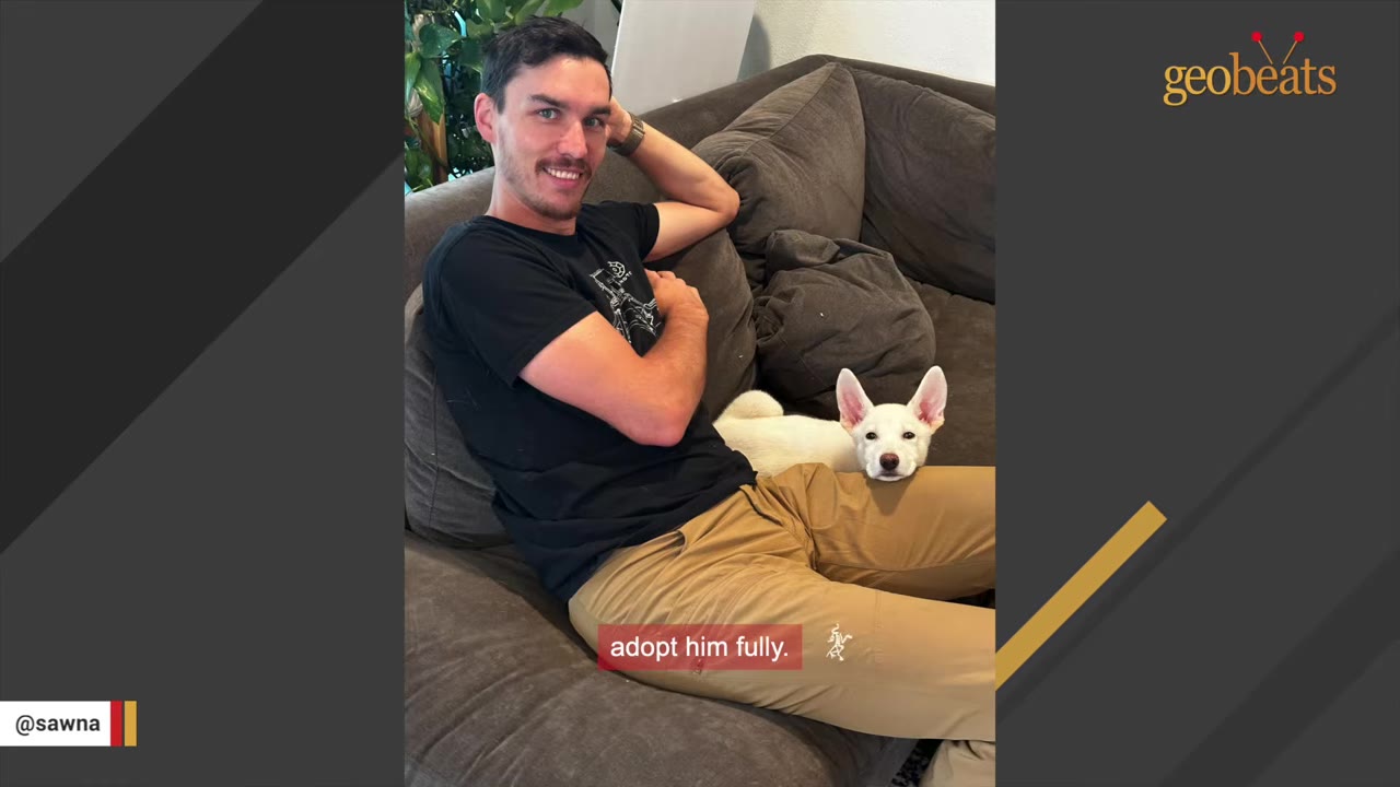 A man in a black t-shirt and khaki pants sits on a brown couch with a small white dog resting its head on his lap.