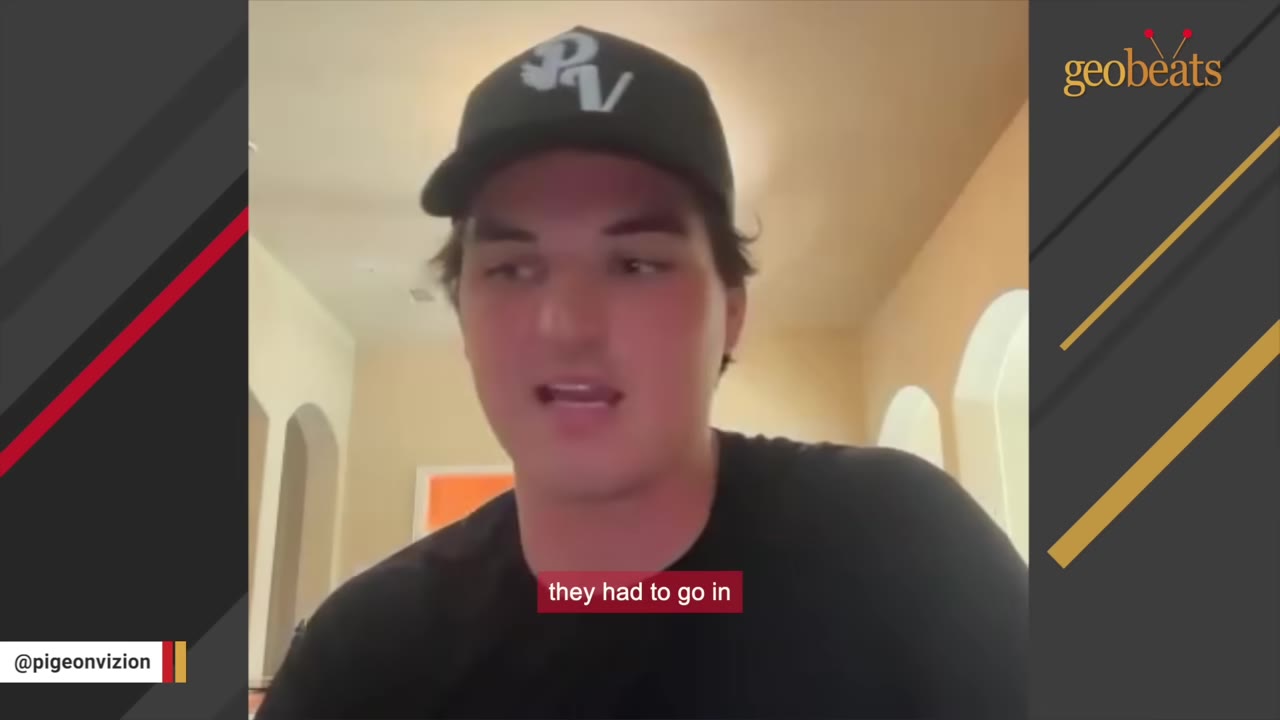 A man wearing a black baseball cap and black t-shirt speaks directly to the camera.