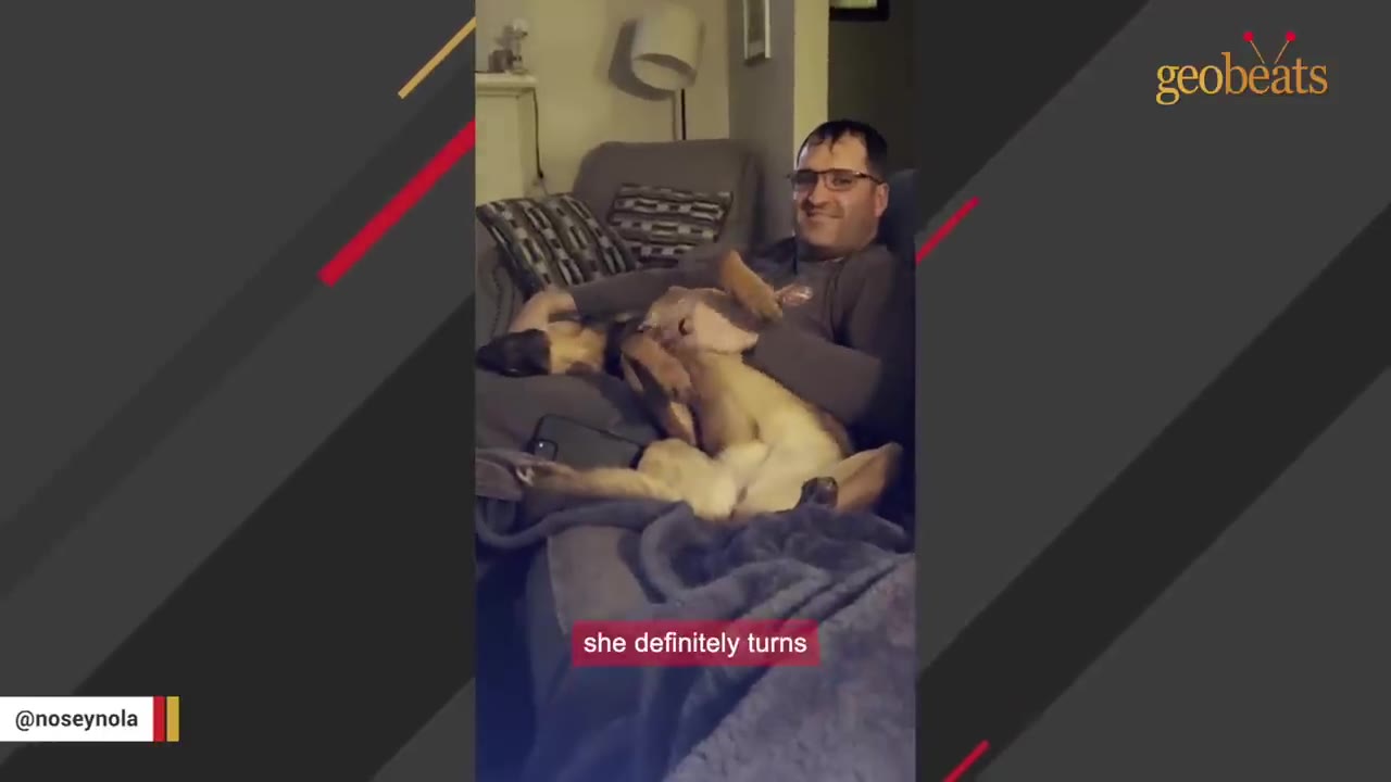 A tan dog lies on its back on a couch, cuddled up with a smiling man wearing glasses.