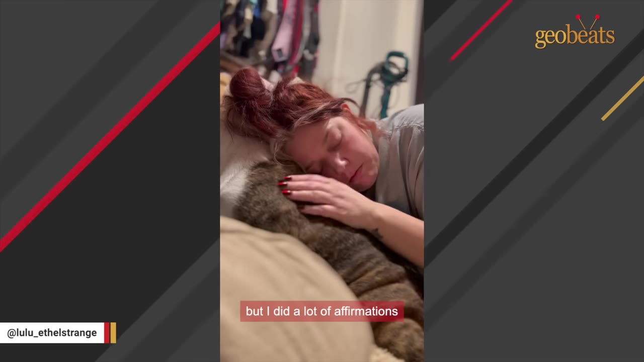 A woman with reddish hair tied up lies next to a brindle dog, gently stroking its back while resting her head near it.