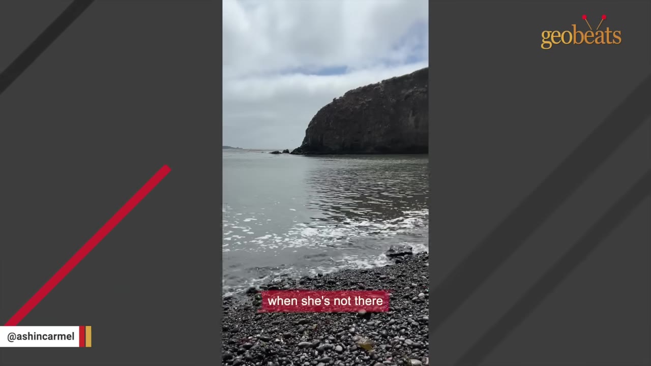 An empty rocky beach and calm cove with a large cliff in the background under a cloudy sky.