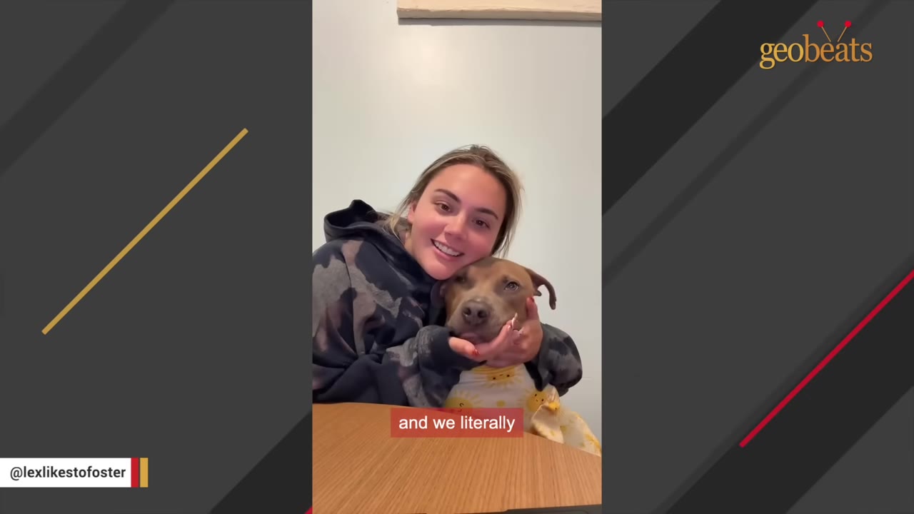 A smiling young woman with blonde hair hugs a brown dog wearing a yellow patterned garment.