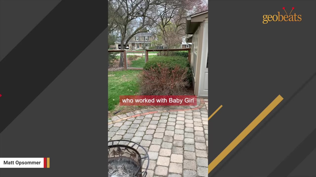 A brick patio in a backyard with a fire pit in the foreground, a bush, and a wooden fence in the background.