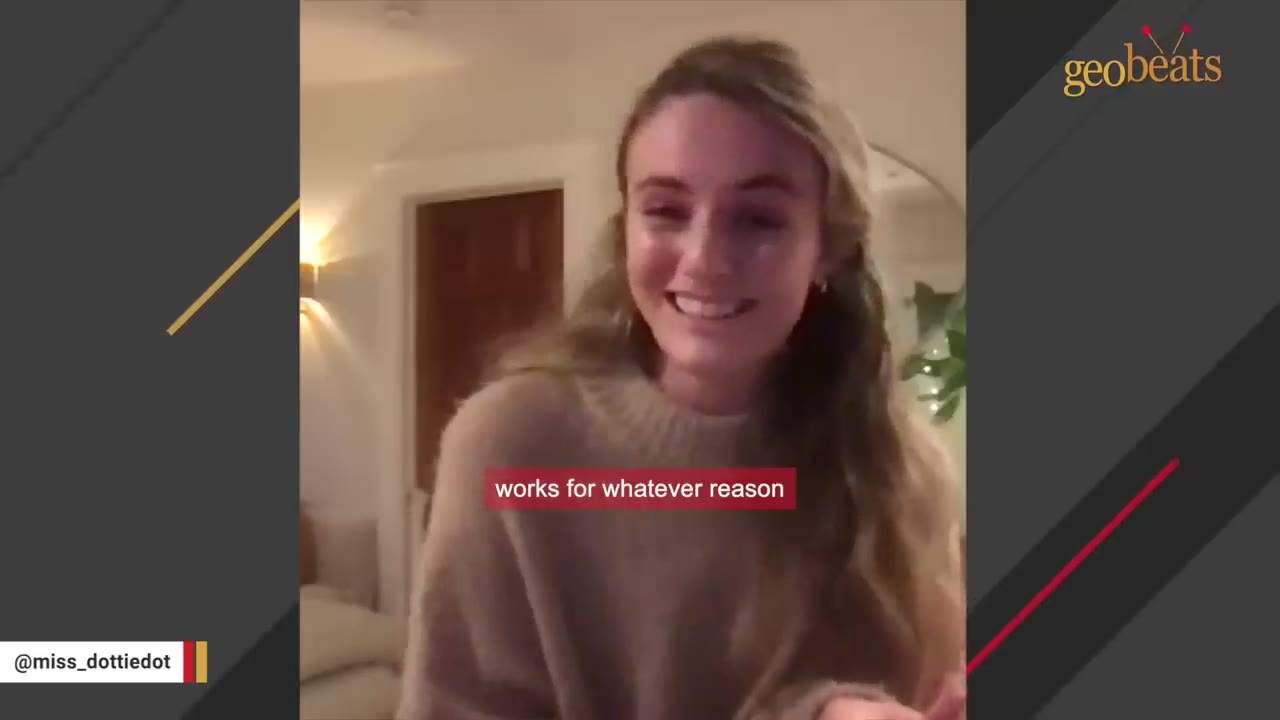 A smiling young woman with long blonde hair wearing a beige sweater speaks directly to the camera in a warmly lit room.